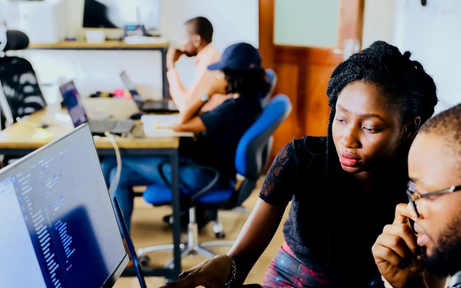 Collega's kijken samen naar een scherm op een werkplek vol laptops
