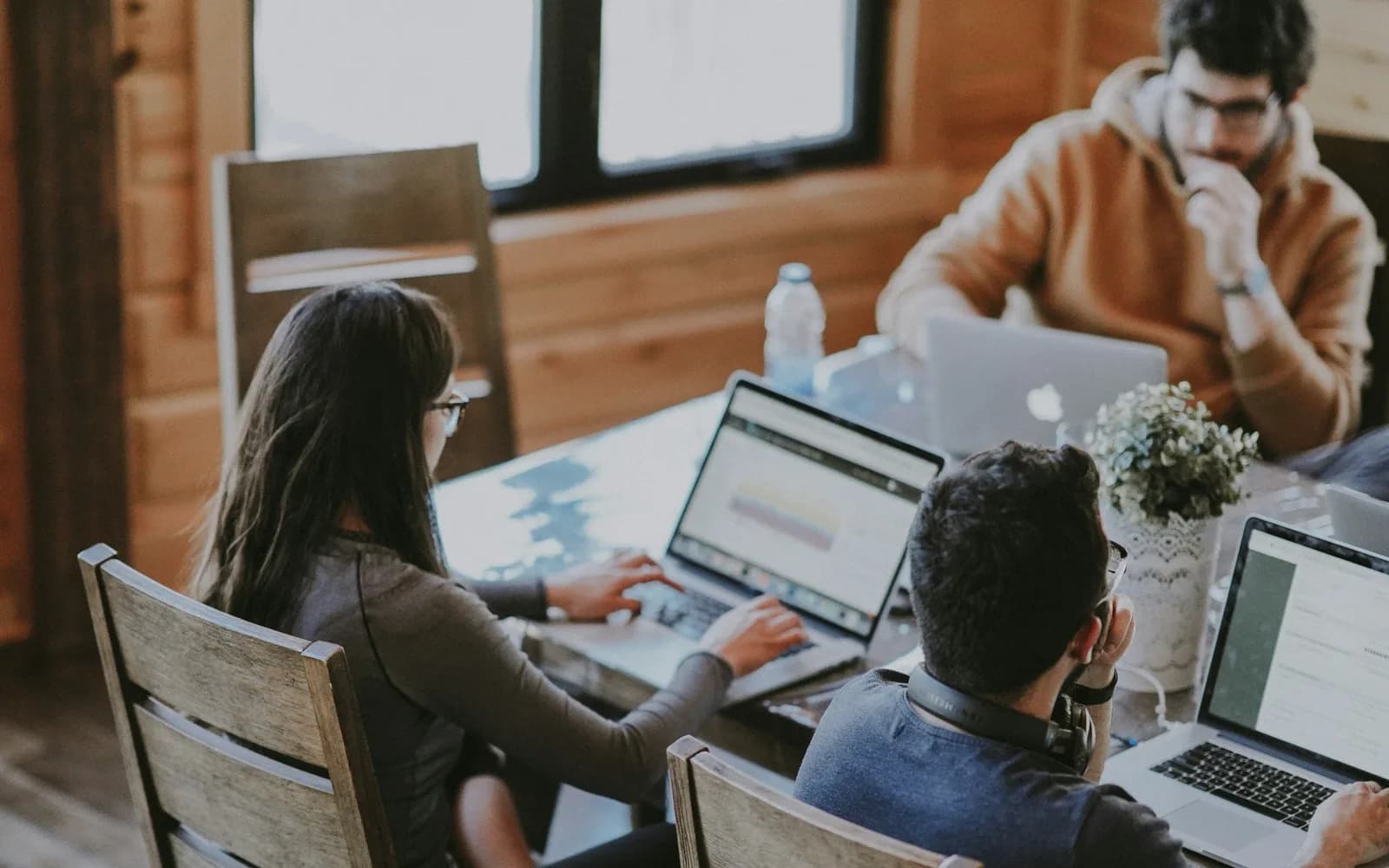 Collega's werken aan laptops aan een houten tafel; op één scherm staat een grafiek