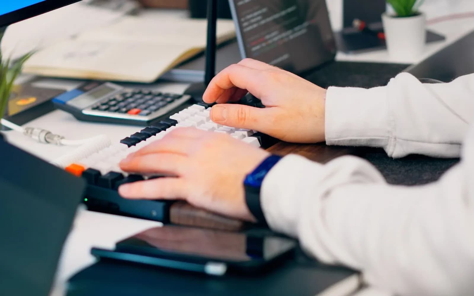 Handen typen op een toetsenbord naast een rekenmachine op een bureau